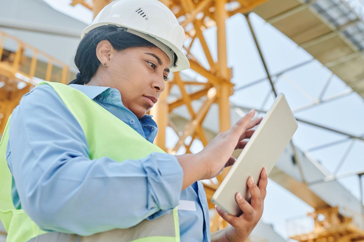 Small contractor in a hard hat checking a tablet on a job site