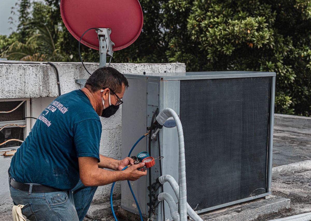 HVAC technician checking an outdoor air-conditioning unit with gauges