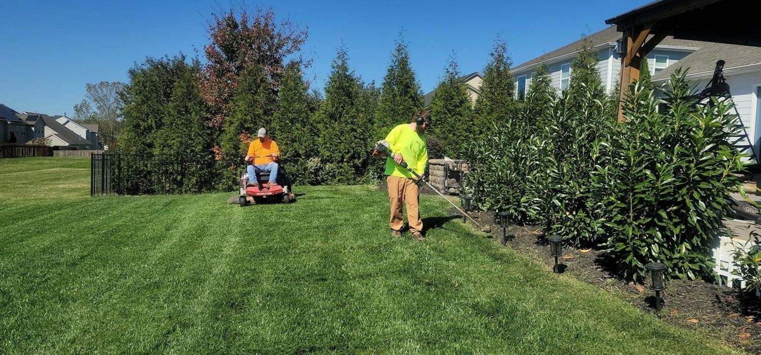 Lawn care crew mowing and trimming a striped residential lawn
