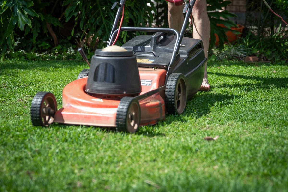 Lawn care worker pushing a mower across green grass